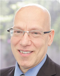 The image shows a man with glasses smiling at the camera.