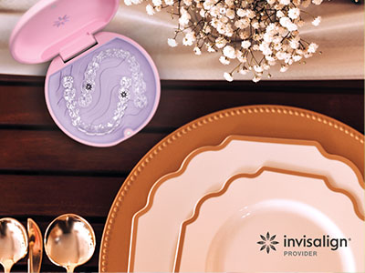 The image shows a collection of tableware including plates, bowls, and utensils displayed on a wooden surface with a pink box containing dental implant parts nearby.