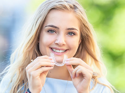 Woman holding up dental appliance with smile.