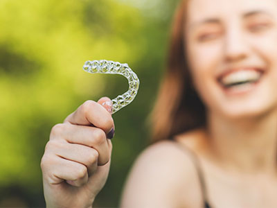 An individual holding up a clear plastic retainer with a smile.