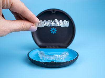 A person s hand holding an open case containing a set of clear dental retainers.