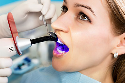 The image features a woman sitting in a dental chair with a dental hygienist using a device to clean her teeth, while she wears a mouthguard and has purple dye on her teeth.