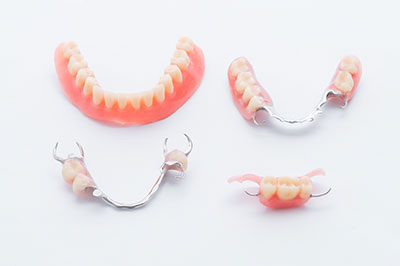 The image displays three pairs of partial dentures with metal clasps, arranged vertically against a white background.