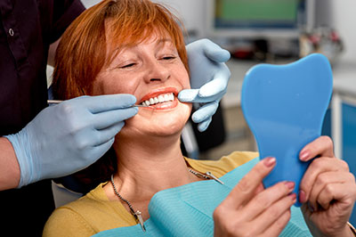 A woman seated at a dental chair with a blue dental impression tray on her lap, receiving dental care from a professional wearing gloves and a face mask.