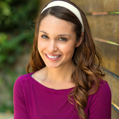 The image features a woman with long brown hair wearing a purple top and a headband, smiling at the camera.