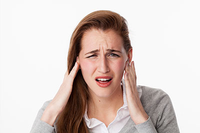 The image shows a young woman with her hand on her head, possibly in pain or discomfort, wearing a gray cardigan, with an expression of concern or distress.