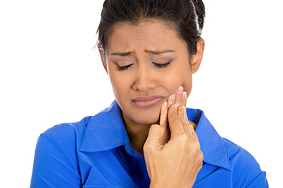 A woman with her eyes closed, holding her face with one hand while looking downward, with a concerned expression.