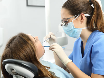 Dental hygienist performing teeth cleaning on patient with dental tools.