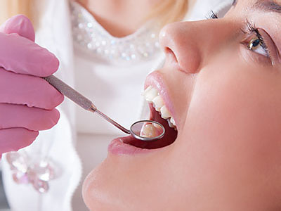 The image shows a dental professional using a dental instrument on a patient s mouth, with the patient wearing protective eyewear and a pink surgical mask.