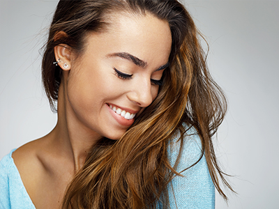 A woman with long hair smiles at the camera while looking downwards.