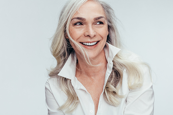 The image shows a woman with short blonde hair, wearing a white shirt, smiling at the camera.