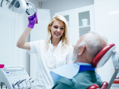 A dental professional assisting an older adult with a medical device, likely during a dental procedure.