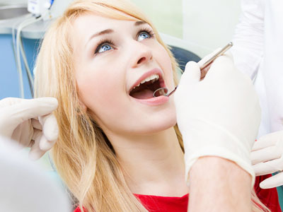 A woman seated in a dental chair receiving dental care, with a dental professional examining her teeth closely.