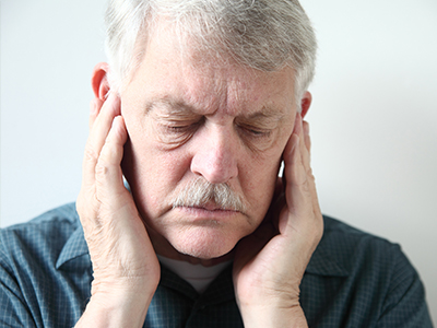 The image shows an elderly man with his eyes closed, holding his face with both hands, appearing to be asleep or resting.